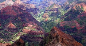 Photo of a deep canyon with red soil and green vegetation