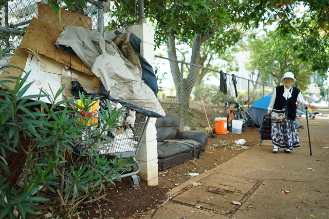 An elderly woman walks past tents located along Beretania Street across from Aala Park with tents and a shopping cart full of garbage. 4 june 2015. photograph Cory Lum/Civil Beat