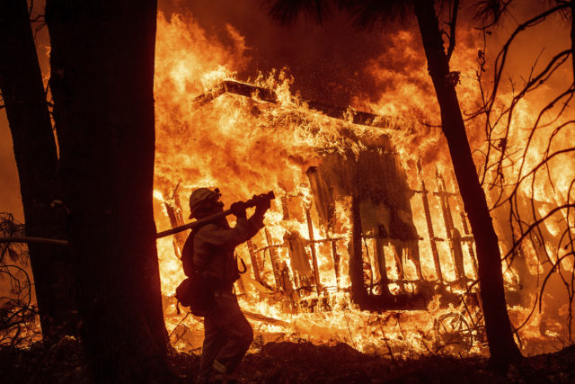 FILE - In this Nov. 9, 2018 file photo, firefighter Jose Corona sprays water as flames from the Camp Fire consume a home in Magalia, Calif. A massive new federal report warns that extreme weather disasters, like California’s wildfires and 2018’s hurricanes, are worsening in the United States. The White House report quietly issued Friday, Nov. 23 also frequently contradicts President Donald Trump. (AP Photo/Noah Berger, File)