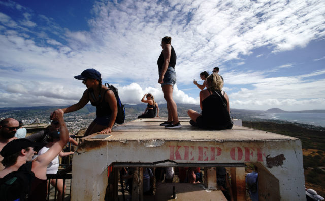 Visitors at Diamond Head summit lookout stand on a concrete bunker disregarding ‘Keep Off’ signs.