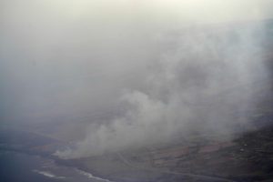 Smoke rises from Lahaina as seen through an airplane window Wednesday, Aug. 9, 2023, in Maui. A large fire consumed the popular tourist location overnight. (Kevin Fujii/Civil Beat/2023)