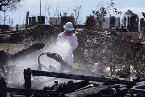 A Truth Excavation employee sprays a soil stabilizer on burned ash and debris Wednesday, Oct. 18, 2023, in Lahaina. Known by its brand name “Soiltac,” once dry, potential hazardous material from burned debris and ash will remain on the ground and not become airborne particles. (Kevin Fujii/Civil Beat/2023)