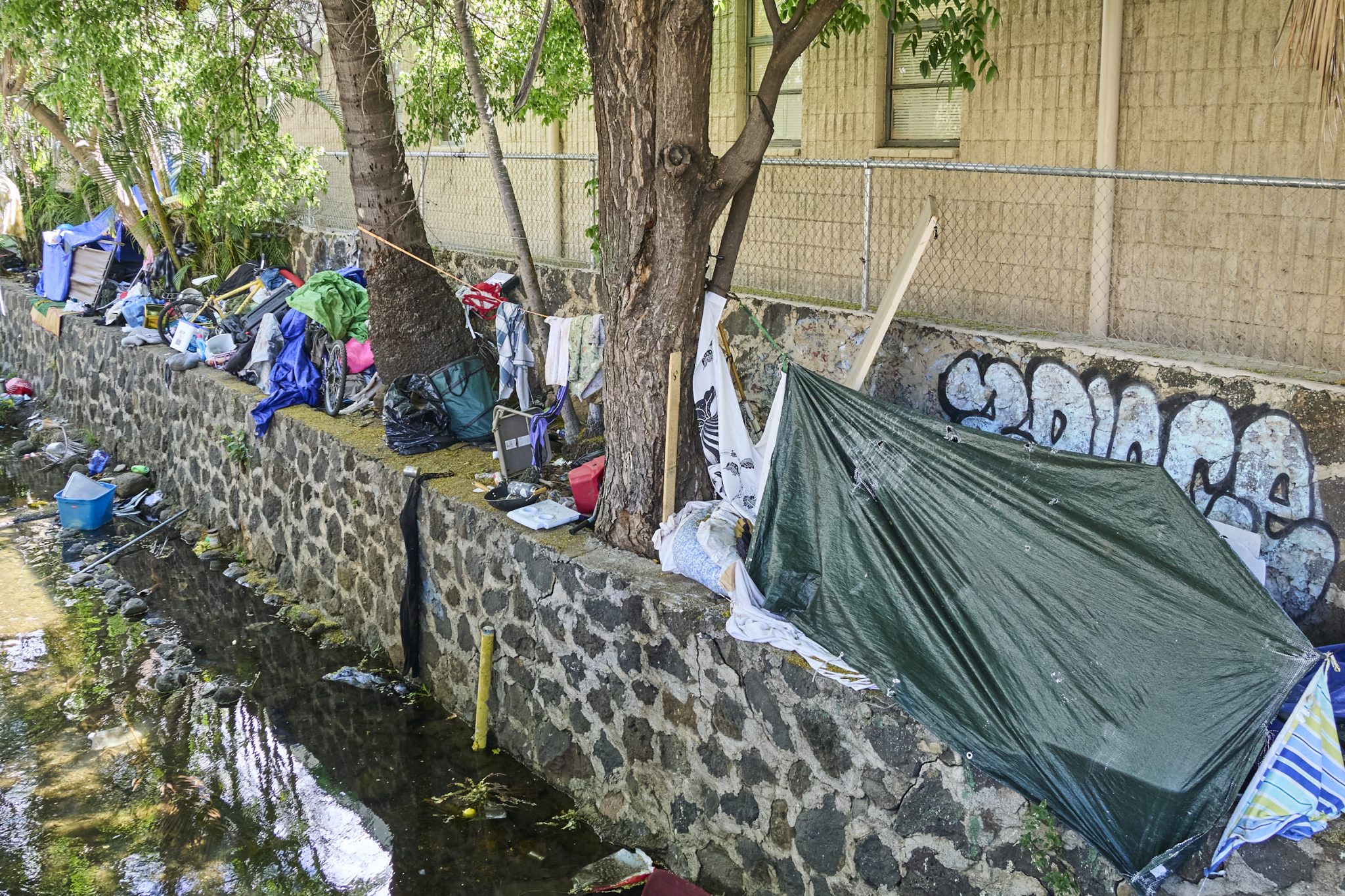 Along the Diamond Head side of Kalakaua Avenue there is a growing homeless encampment dotted along the stream that parallels the famously named street. Some of the tents surround a Bus stop within eyesight of the local Jack in the Box. The assortment of trash ranges from Shopping Carts to displaced Yeti water flasks and everything in between. Photographed Wednesday June 12, 2024(David Croxford/Civil Beat/2024)