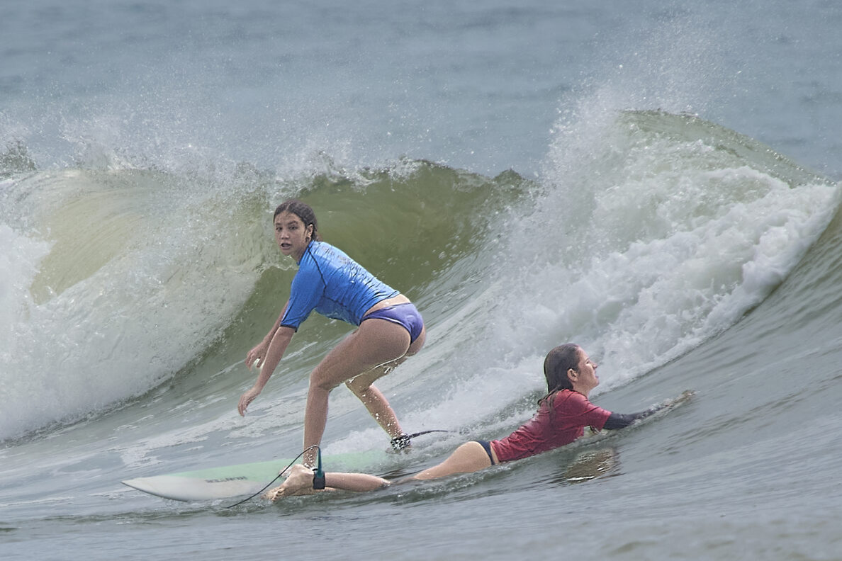 High School surfing started its season at Ala Moana Bowls on Saturday October 26th, 2024 with 17 schools competing in the day long event. In the girls short board event Kara Watson (Blue) takes off on a wave as Solbee Ahina (Red) paddles out.(David Croxford/Civil Beat/2024)