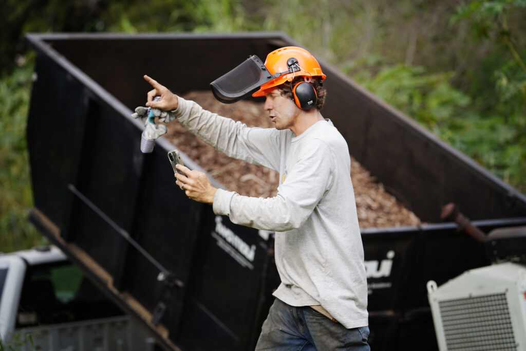 Mālama Kula Executive Director Kyle Ellison (orange helmet) uses his phone to update Maui’s Upcountry recovery process Friday, Nov. 8, 2024, in Kula. This mostly residential, non-tourist area was hit with a fire the same day as Lahaina on Aug. 8, 2023. (Kevin Fujii/Civil Beat/2024)