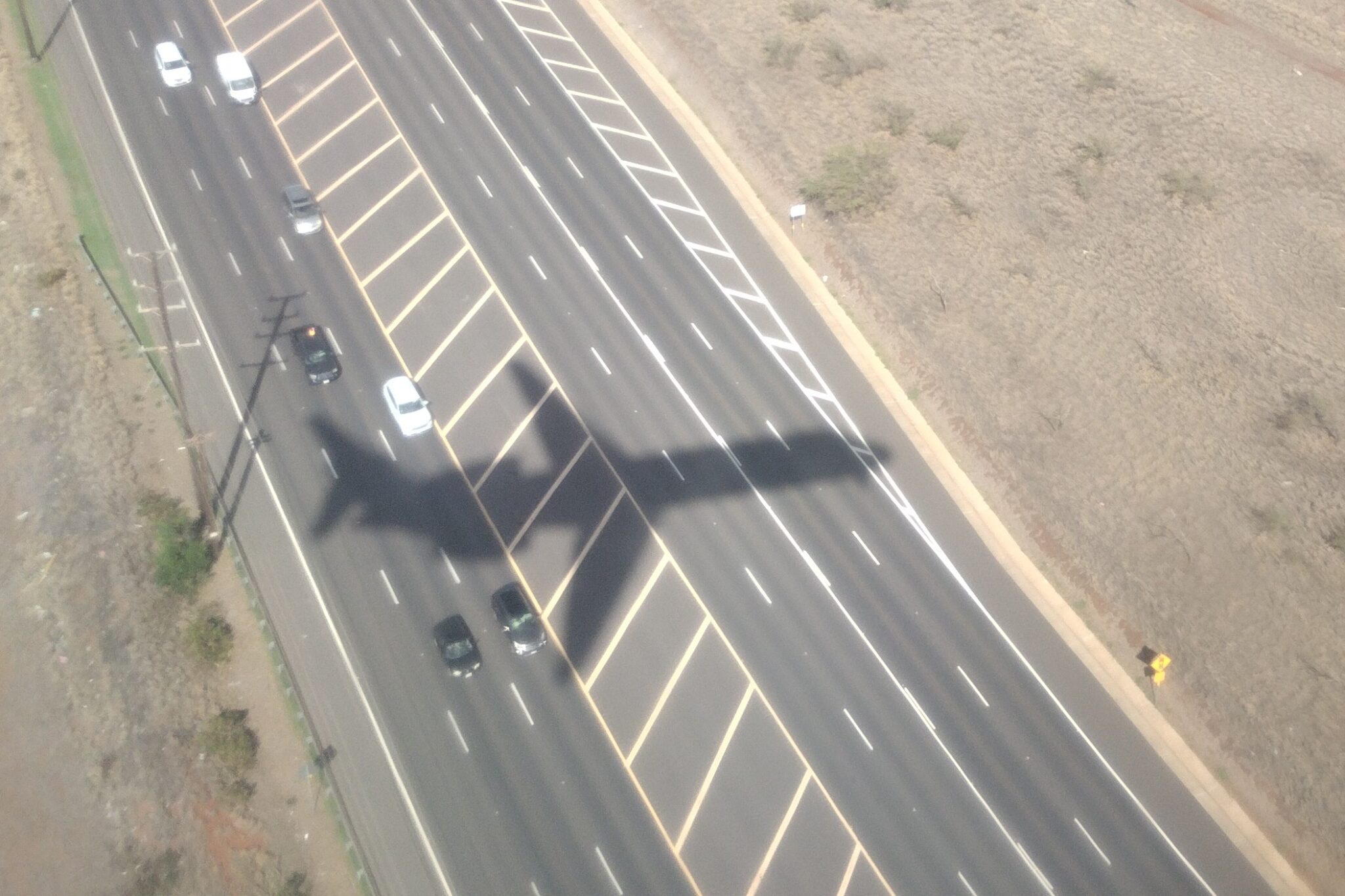 The shadow of a Rolls-Royce-powered Boeing 717-200 used by Hawaiian Airlines for interisland flights crosses Hana Highway during its descent to land at Kahului Airport on Maui. (Léo Azambuja/Civil Beat/2024)