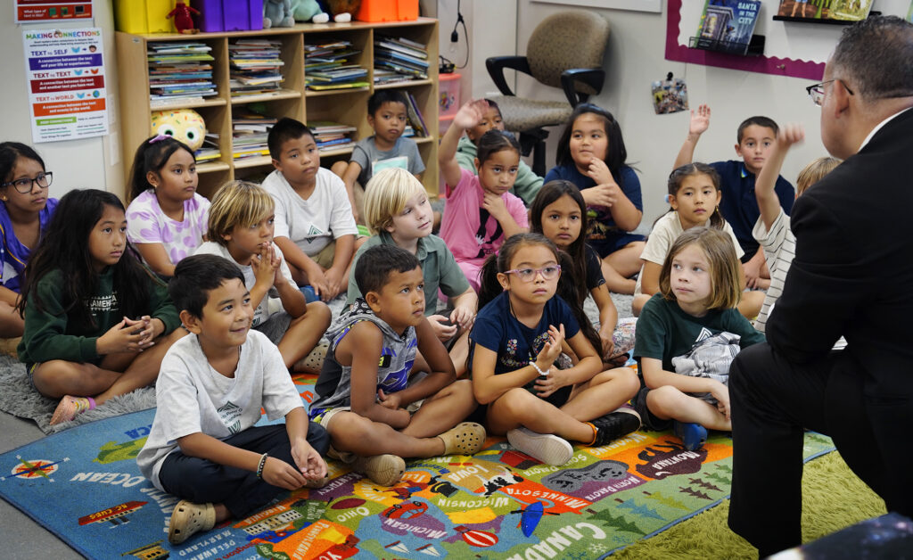 U.S. Department of Education Sec. Miguel Cardona, left, talks with Cassie Coonradt’s Kamehameha III Elementary School second-grade students Friday, Dec. 6, 2024, in Lahaina. (Kevin Fujii/Civil Beat/2024)