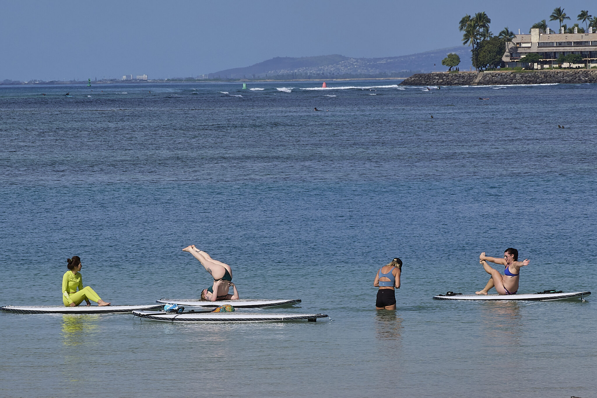 A group of ladies enjoys practice Yoga moves on Stand Up Paddle Boards in the shallow portions of the lagoon at Ala Moana Park (David Croxford/Civil Beat/2025)
