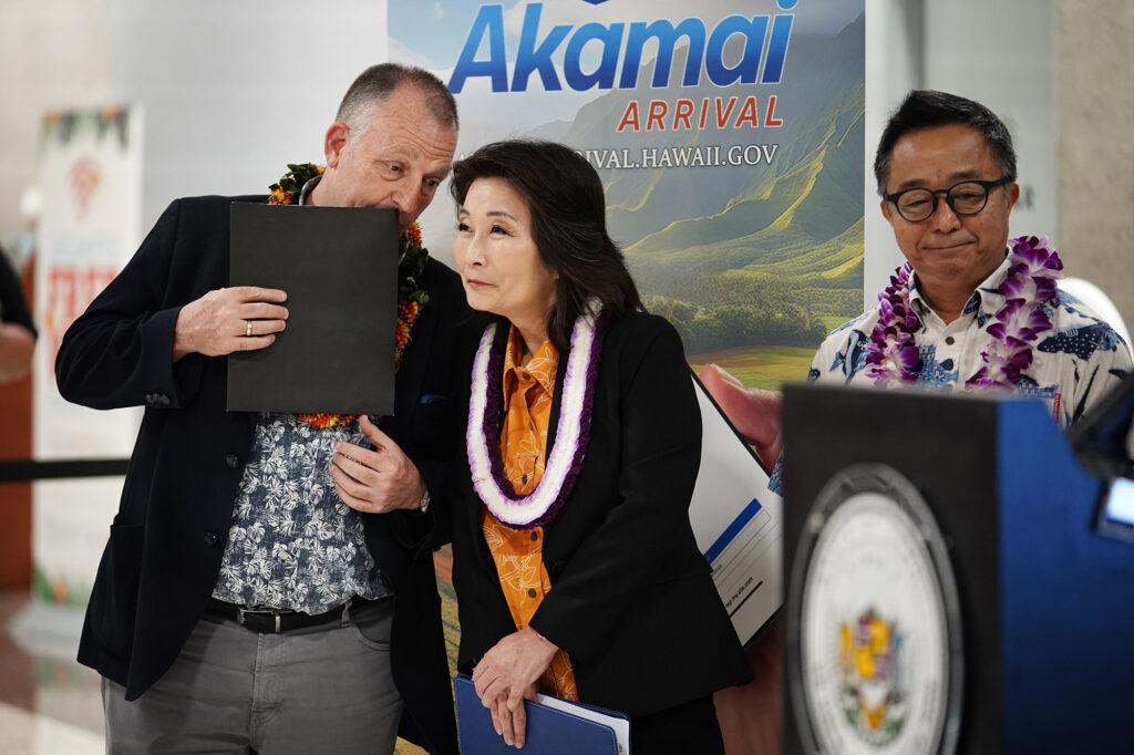 Gov. Josh Green whispers to Lt. Gov. Sylvia Luke while Sen. Glenn Wakai looks on during the news briefing for digitizing Hawaiʻi Department of Agriculture’s plant and animal declarations Monday, Feb. 24, 2025, at Daniel K. Inouye International Airport in Honolulu. (Kevin Fujii/Civil Beat/2025)