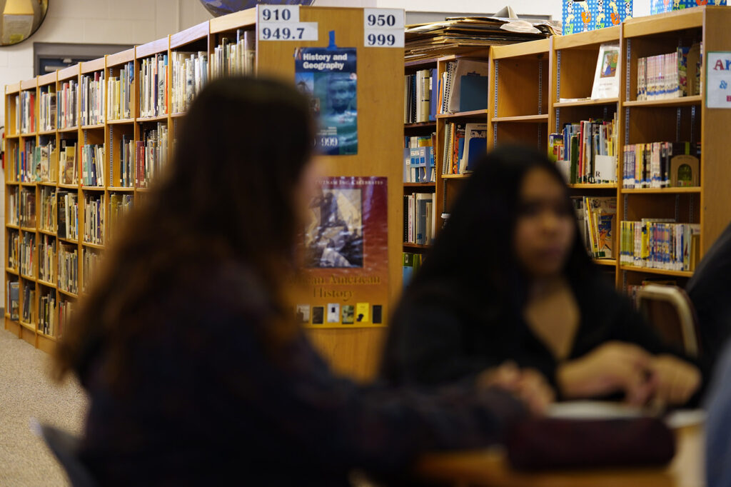 Bookcases filled with books line up behind Waiākae High School students while they listen to librarian Leslie Fukushima Monday, March 10, 2025, in Hilo. (Kevin Fujii/Civil Beat/2025)