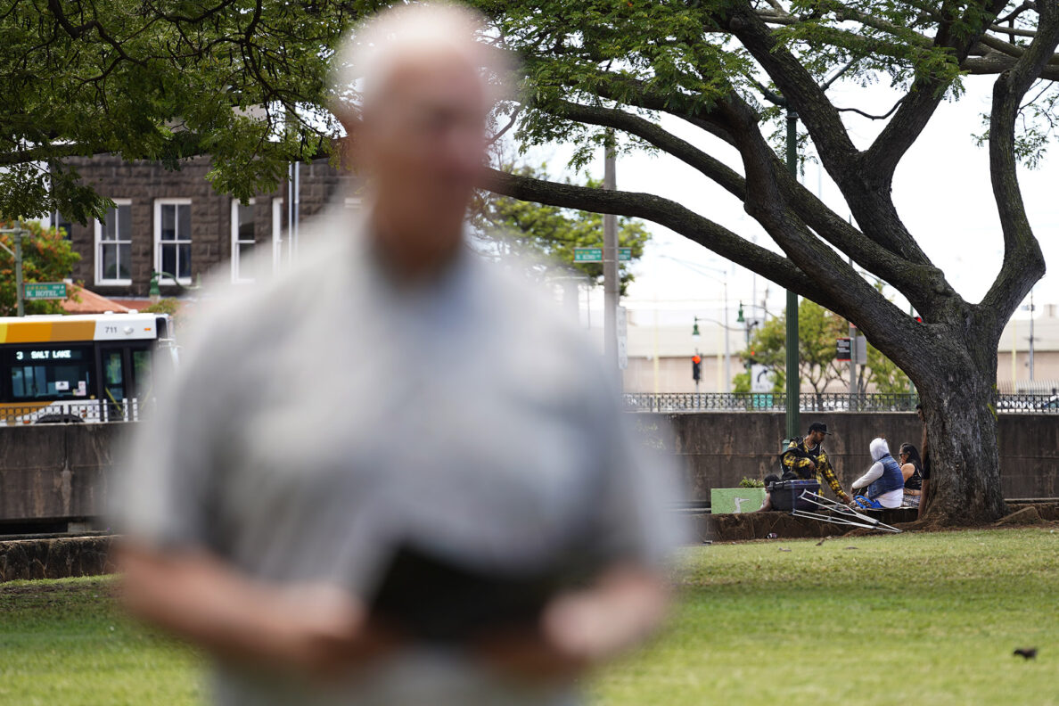 People loiter on the edges of A’ala Park as Mayor Rick Blangiardi waits to speak during his request for more homeless advocates Tuesday, April 15, 2025, at A’ala Park in Honolulu. (Kevin Fujii/Civil Beat/2025)