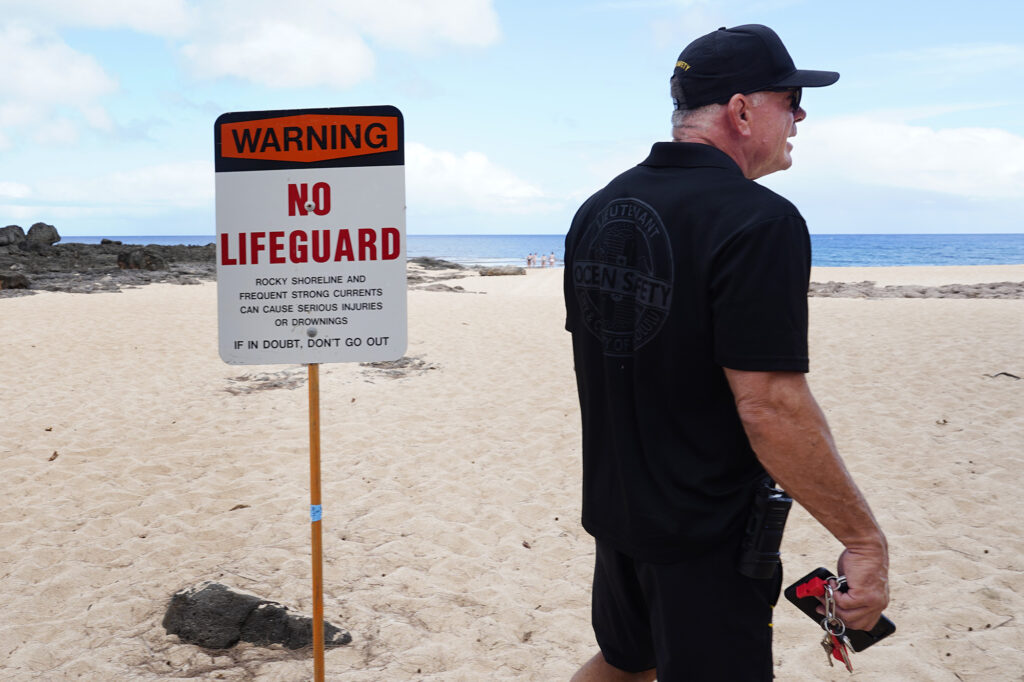 Honolulu City and County Ocean Safety Lt. Kerry Atwood stands near a “Warning No Lifeguard” sign at Ke Ike Beach Monday, June 16, 2025, on the North Shore of Oʻahu. (Kevin Fujii/Civil Beat/2025)