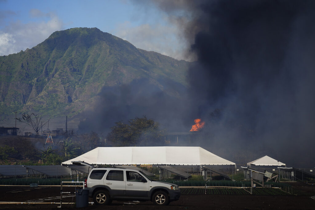 A Māʻili vegetation fire reaches a structure Sunday, July 6, 2025, in Waiʻanae. A mandatory evacuation order was issued mauka of Kulaaupuni Road. According to the Honolulu Fire Department, the fire is reported to be 75% contained at 7:25 p.m.. Almost 100 acres have burned, with some structures damaged and a woman transported to the hospital with burns and smoke inhalation. (Kevin Fujii/Civil Beat/2025)