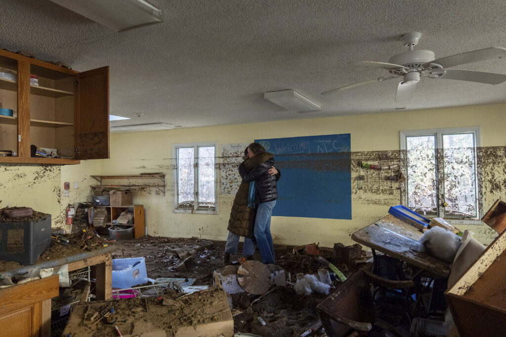Nicole Schoychid, left, and Rebekah Canu, co-founders of Wildwood Agile Leaning Center, embrace inside the schoolhouse, which was damaged by flooding in Hurricane Helene, as they are surrounded by debris and mud, Thursday, Dec. 5, 2024, in Boone, N.C. The school had to compete against many other organizations and businesses vying for their own space in Boone after Helene damaged the town, creating a “bottleneck” from demand, Schoychid says. (AP Photo/Stephanie Scarbrough)