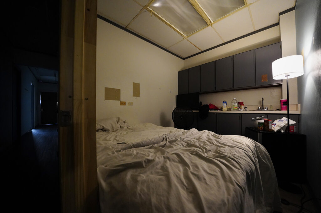 A renter shows his room at 1136 Union Mall Friday, Sept. 26, 2025, in Honolulu. The space fits a double-size bed and is stuffy without ventilation. The Union Plaza office building has been mostly converted to residential rental units. (Kevin Fujii/Civil Beat/2025)