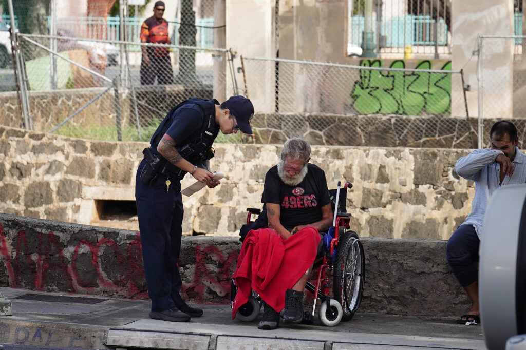 A Honolulu Police Department officer writes a citation to Jerry Clark Friday, Oct. 16, 2025, in Honolulu. Clark is homeless and stays on the streets in Chinatown. (Kevin Fujii/Civil Beat/2025)