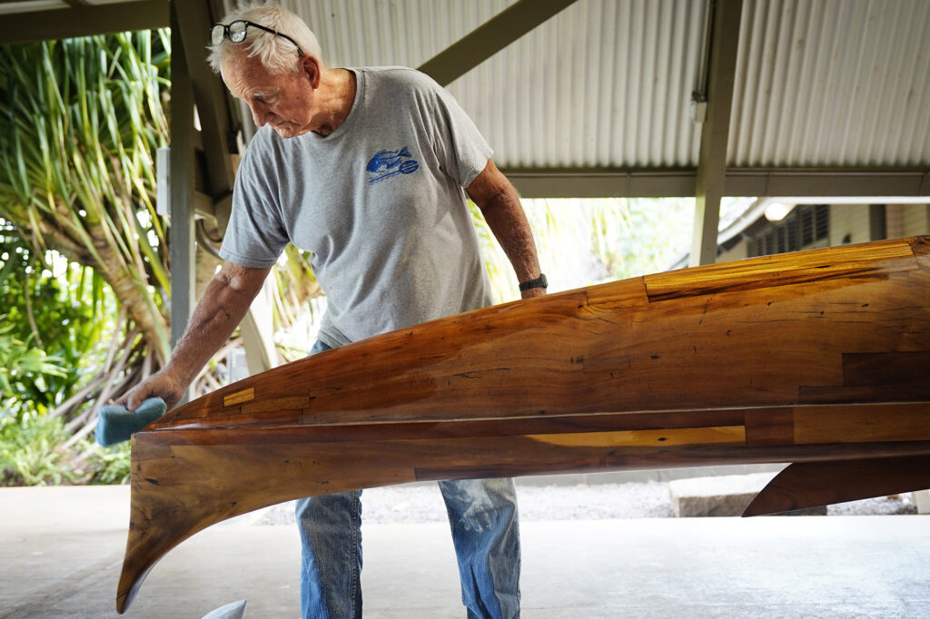 Tay Perry smoothes out the final coat on Prince Jonah Kūhiō Kalanianaʻole’s a‘a Monday, Nov. 3, 2025, at the Bishop Museum in Honolulu. The 40-foot racing canoe will return to the water for the first time in more than a decade. (Kevin Fujii/Civil Beat/2025)