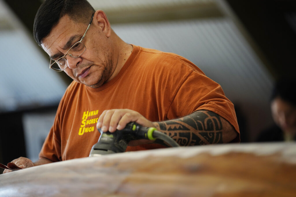 Ryan Olivares prepares Prince Jonah Kūhiō Kalanianaʻole’s a‘a for its final coat Monday, Nov. 3, 2025, at the Bishop Museum in Honolulu. The 40-foot racing canoe will return to the water for the first time in more than a decade. (Kevin Fujii/Civil Beat/2025)