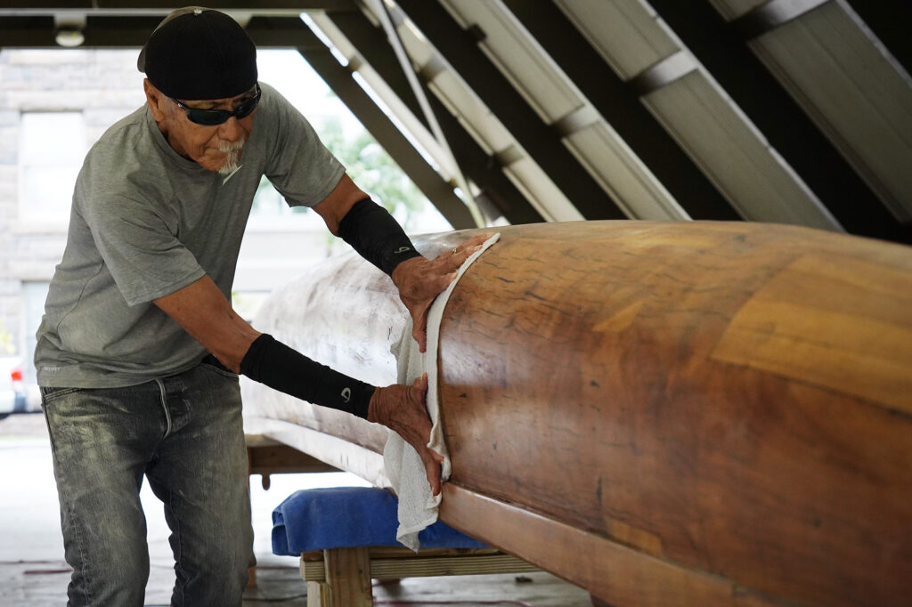 Billy Richards wipes down Prince Jonah Kūhiō Kalanianaʻole’s a‘a before applying its final coat Monday, Nov. 3, 2025, at the Bishop Museum in Honolulu. The 40-foot racing canoe will return to the water for the first time in more than a decade. (Kevin Fujii/Civil Beat/2025)