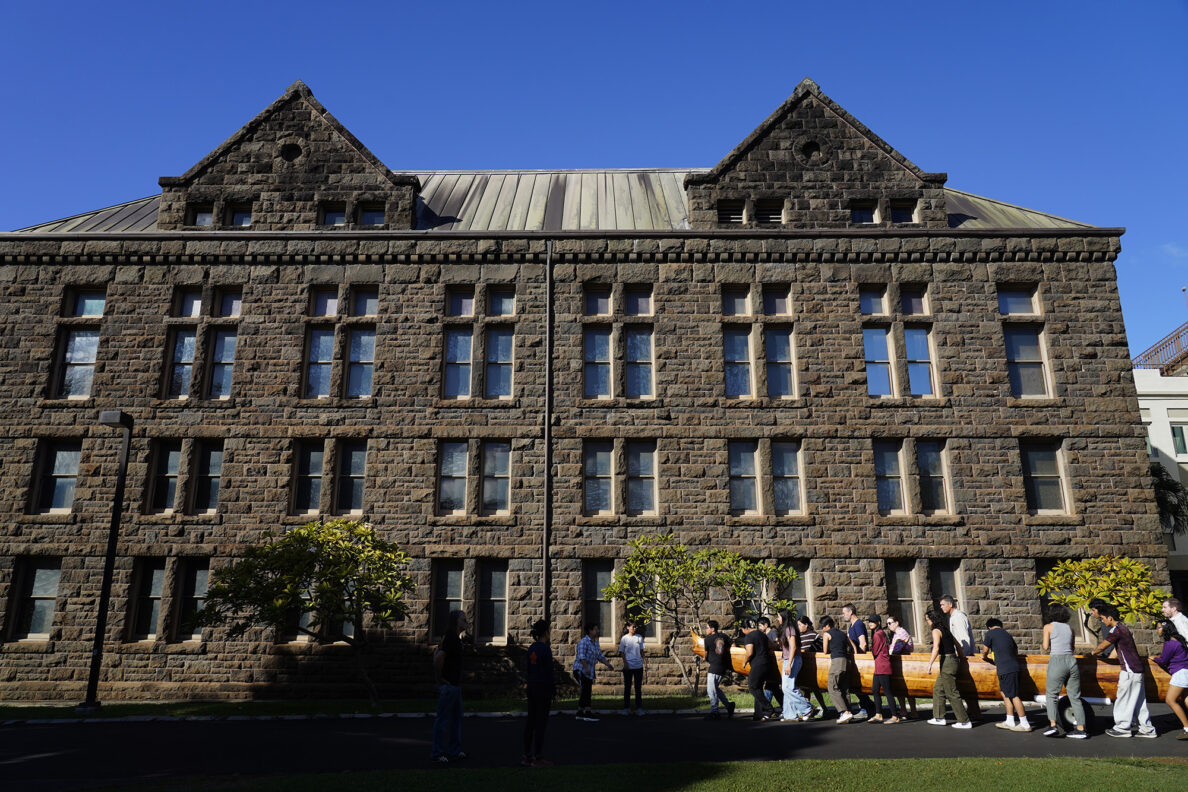 Farrington High School students help move Prince Kūhiō’s A‘a at Bishop Museum to to a trailer Friday, Nov. 7, 2025, in Honolulu. It’s being moved to Ke‘ehi Lagoon for a ceremonial blessing and paddle. (Kevin Fujii/Civil Beat/2025)