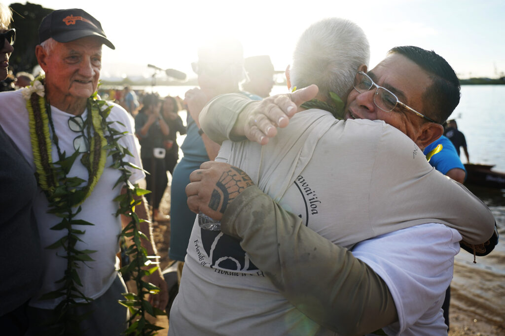 Tay Perry, from left, looks on as Billy Richards hugs Perry’s apprentice Ryan Olivares after the A‘a’s inaugural paddle at Ke‘ehi Lagoon Saturday, Nov. 8, 2025, in Honolulu. (Kevin Fujii/Civil Beat/2025)