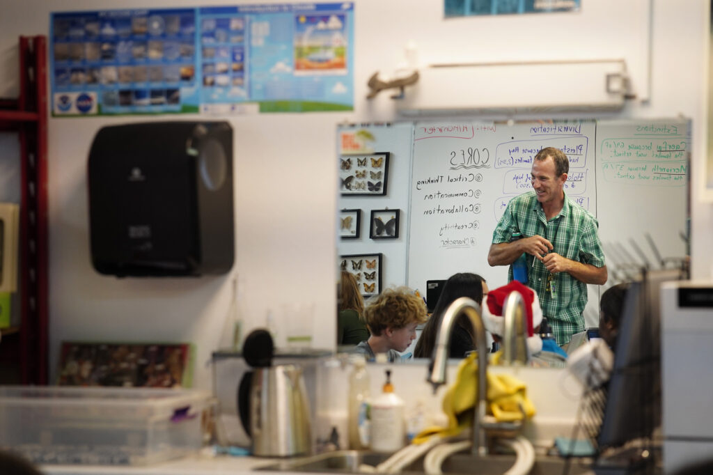 Hawaiʻi Technology Academy Kauaʻi teacher Drew Cohick talks with students during an advisory period Wednesday, Nov. 19, 2025, in a Līhuʻe office park. Cohick is reflected in a mirror mounted on a wall. (Kevin Fujii/Civil Beat/2025)