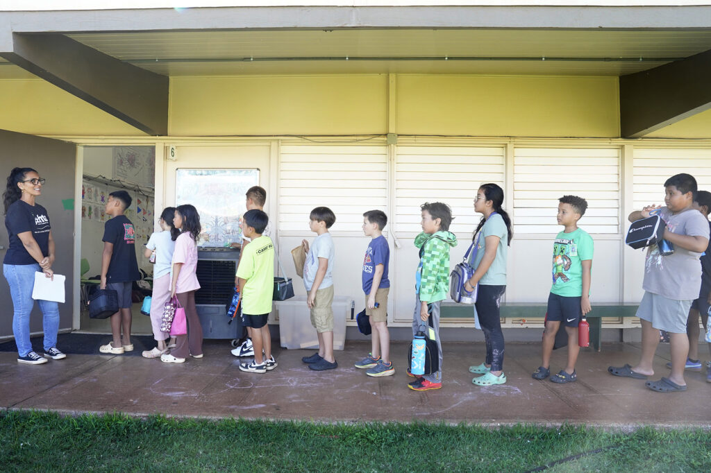 4th graders form a a line in front of their teacher at the entrance to a classroom.