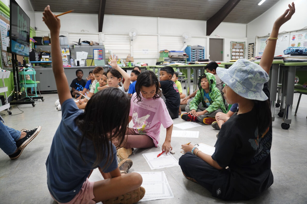Hawaiʻi Technology Academy 4th graders Sera Witte, left,  and Olivia Xu raise their hands during an in-class assignment Tuesday, Dec. 2, 2025, in ʻEwa Beach. (Kevin Fujii/Civil Beat/2025)