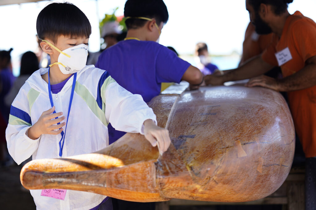Kapālama Elementary School 4th grader Changqiu Wang sands Keaolewao Kalihi wooden wa‘a during the Ho‘ākea Honolulu hands-on learning and experiencing event centered around traditional Hawaiʻian navigation and voyaging canoes Wednesday, Dec. 3, 2025, in Honolulu. Hawaiʻian voyaging traditions, cultural practices and ʻāina-based learning pairs with DOE curriculum to create a “Navigator Mindset”. (Kevin Fujii/Civil Beat/2025)