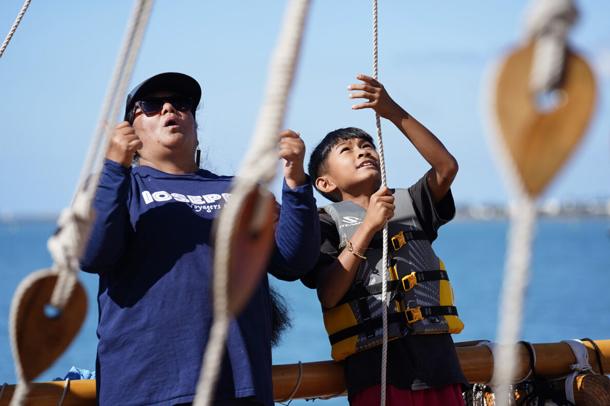 Anna Logan with BYU Hawaiʻi’s Iosepa voyaging canoe cheers on Kapālama Elementary School 4th grader Rykin McKee as he raises the sail during the Ho‘ākea Honolulu hands-on learning and experiencing event centered around traditional Hawaiʻian navigation and voyaging canoes Wednesday, Dec. 3, 2025, in Honolulu. Hawaiʻian voyaging traditions, cultural practices and ʻāina-based learning pairs with DOE curriculum to create a “Navigator Mindset”. (Kevin Fujii/Civil Beat/2025)
