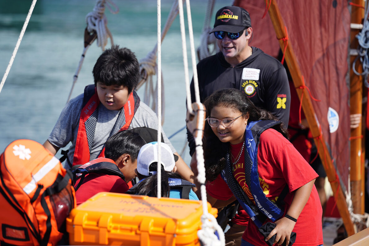Lele Aloha’s Ka‘anapu Kalama-Jacobsen, in black, guides Kalihi Kai Elementary School 4th graders to move the hoe uli (rudder paddle) on the Mānaiakalani voyaging canoe during the Ho‘ākea Honolulu hands-on learning and experiencing event centered around traditional Hawaiʻian navigation and voyaging canoes Wednesday, Dec. 3, 2025, in Honolulu. Hawaiʻian voyaging traditions, cultural practices and ʻāina-based learning pairs with DOE curriculum to create a “Navigator Mindset”. (Kevin Fujii/Civil Beat/2025)