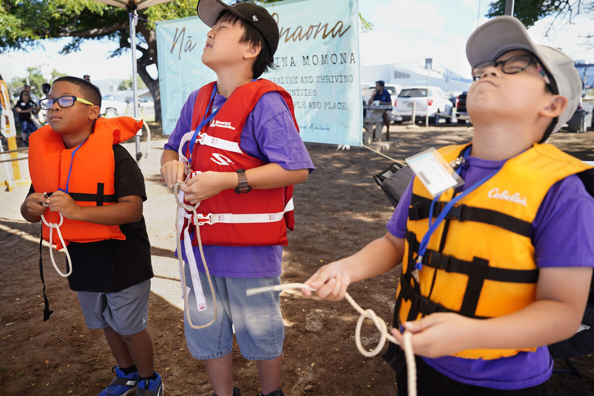 Kapālama Elementary School 4th graders Rixon Allgood-Pascual, from left, Johnny Chen and Kian Reyes close their eyes to mimic nighttime while trying square knots during the  Ho‘ākea Honolulu hands-on learning and experiencing event centered around traditional Hawaiʻian navigation and voyaging canoes Wednesday, Dec. 3, 2025, in Honolulu. Hawaiʻian voyaging traditions, cultural practices and ʻāina-based learning pairs with DOE curriculum to create a “Navigator Mindset”. (Kevin Fujii/Civil Beat/2025)