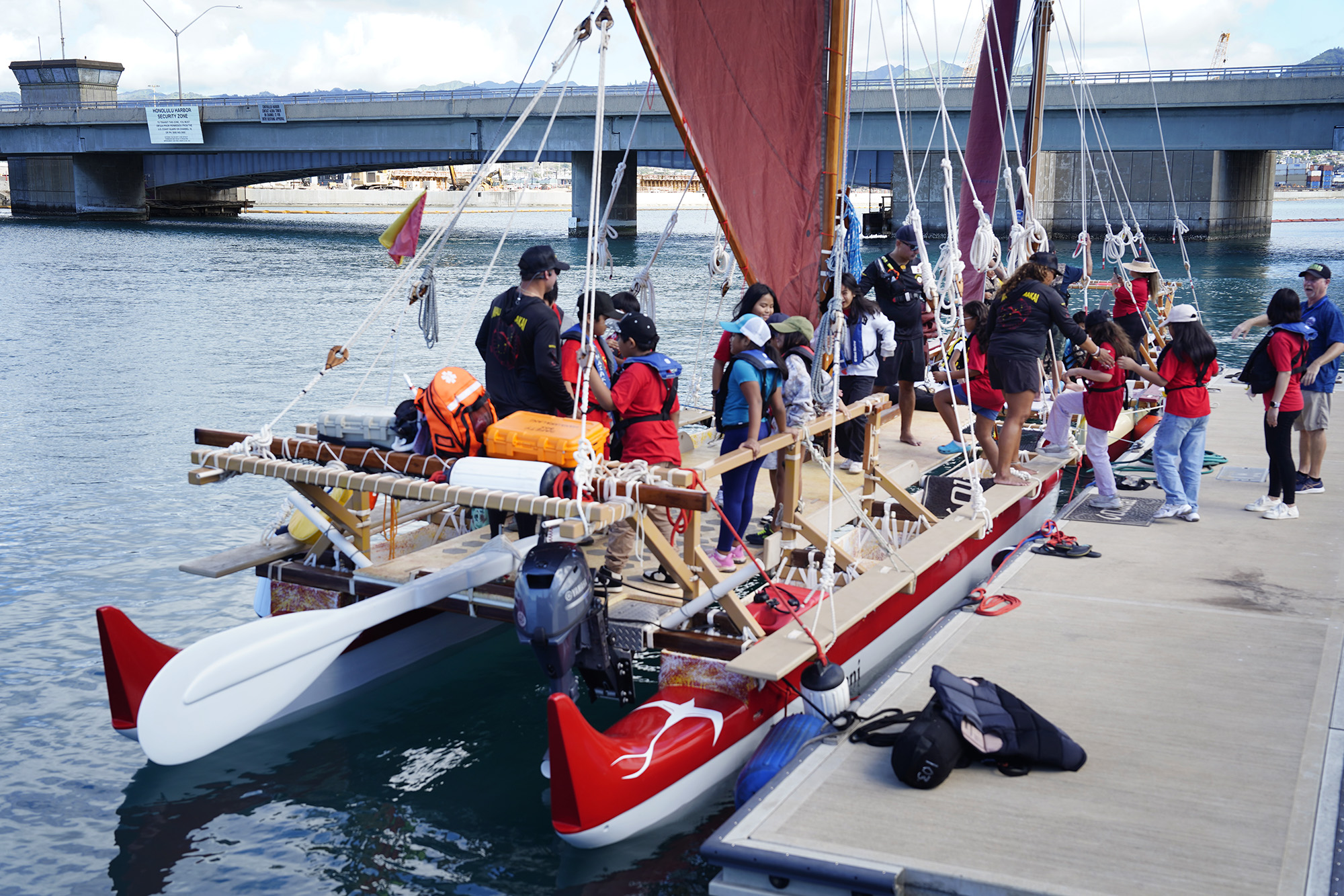 Kalihi Kai Elementary School 4th graders climb aboard Lele Aloha’s Mānaiakalani voyaging canoe during the Ho‘ākea Honolulu hands-on learning and experiencing event centered around traditional Hawaiʻian navigation and voyaging canoes Wednesday, Dec. 3, 2025, in Honolulu. Hawaiʻian voyaging traditions, cultural practices and ʻāina-based learning pairs with DOE curriculum to create a “Navigator Mindset”. (Kevin Fujii/Civil Beat/2025)