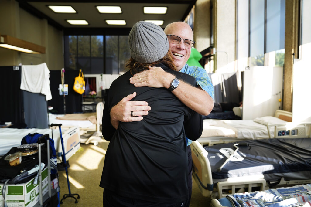 Scott Miscovich re-connects with William Coward during  his rounds at the A‘ala Respite Center Monday, Dec. 8, 2025, in Honolulu. The former bank building turned medical facility is attached to a kauhale to help homeless get well and back on their feet. Miscovich and Coward are physicians who once worked together. (Kevin Fujii/Civil Beat/2025)