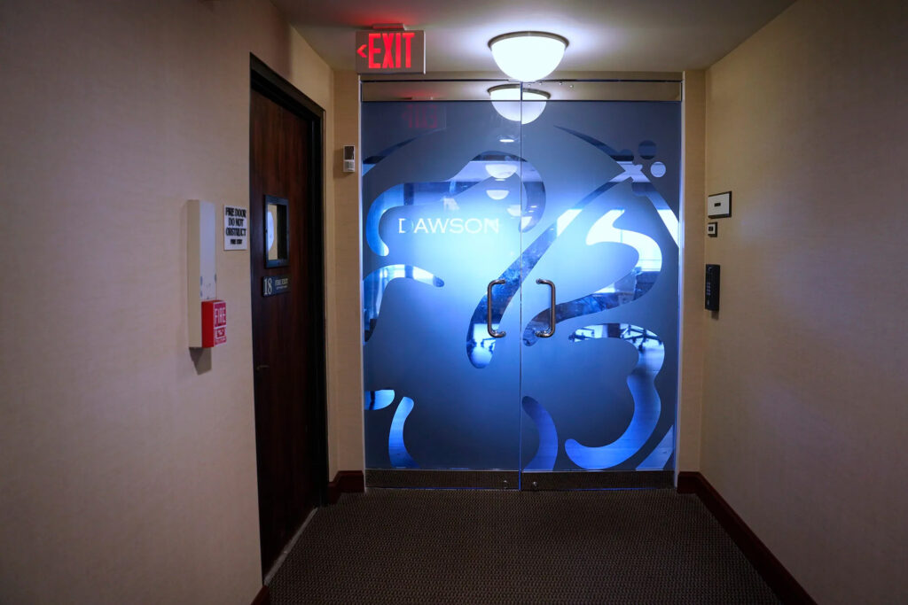 In an office building, a hallway leads to a glass door with an ornate floral design in frosted glass and the word “DAWSON” on it