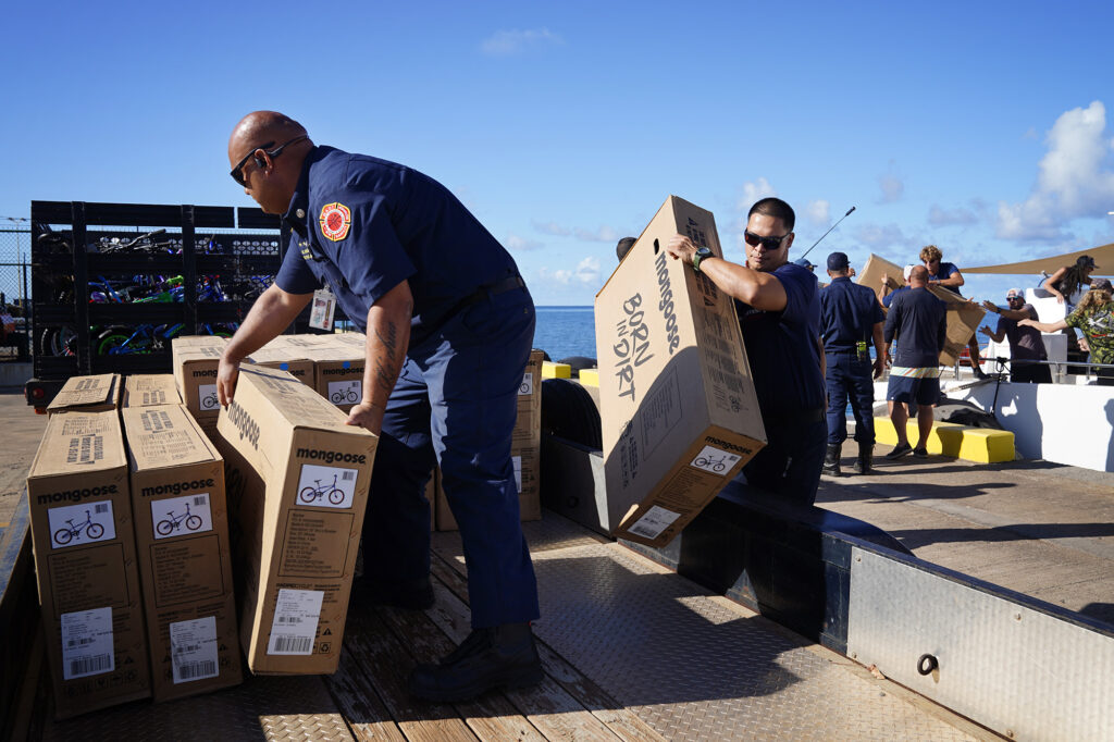 Kaunakakai Fire Station fire fighters and Maui County employees load new, unboxed bicycles for Jim Falk’s annual Christmas Kids Bike Build Wednesday, Dec. 10, 2025, at Molokaʻi Wharf in Kaunakakai. Approximately 450 new bicycles are built and will distributed to keiki in Maui County. (Kevin Fujii/Civil Beat/2025)