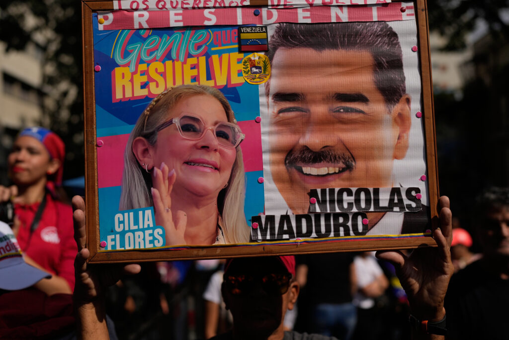 A government supporter holds photos of Venezuelan President Nicolas Maduro and first lady Cilia Flores at a women's march to demand their return in Caracas, Venezuela, Tuesday, Jan. 6, 2026, three days after U.S. forces captured them. (AP Photo/Matias Delacroix)