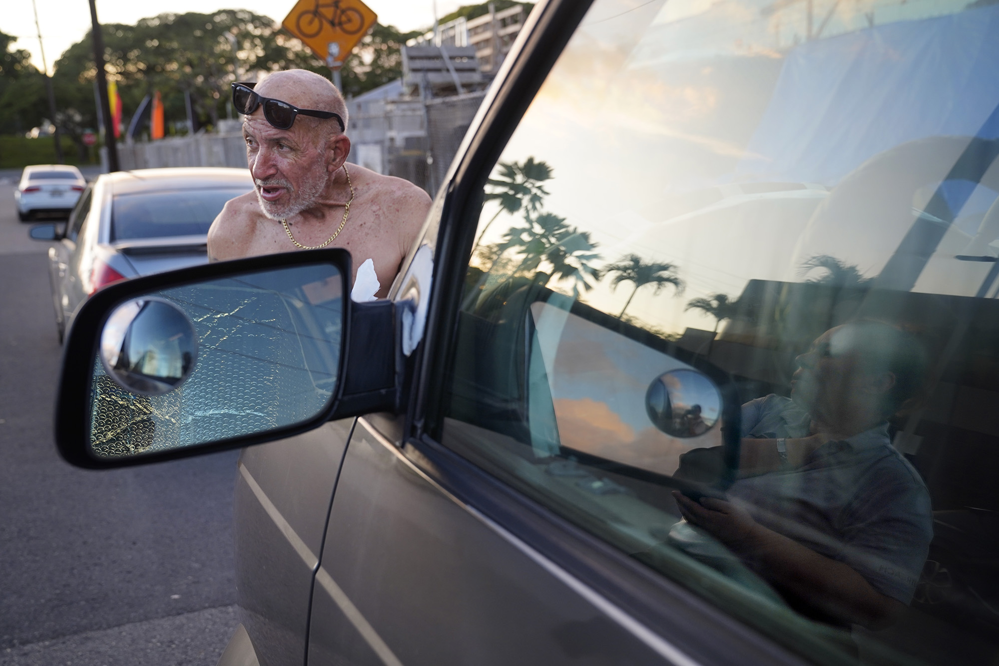 Joseph Vascocelles talks story with IHS’ Sarah Rodrigues, reflected on window, Monday, Jan. 26, 2026, in Honolulu. He lives in this bus and is the janitor at Marmol Hawaii which he parks next to. (Kevin Fujii/Civil Beat/2026)