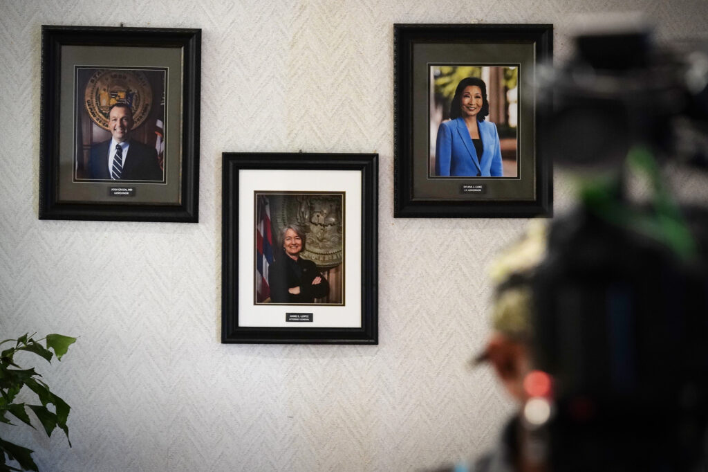 Official State of Hawaiʻi portraits of Gov. Josh Green, upper left, and Lt. Gov. Sylvia Luke are placed above Attorney General Anne Lopez photographed Friday, Feb. 13, 2026, in Honolulu. (Kevin Fujii/Civil Beat/2026)
