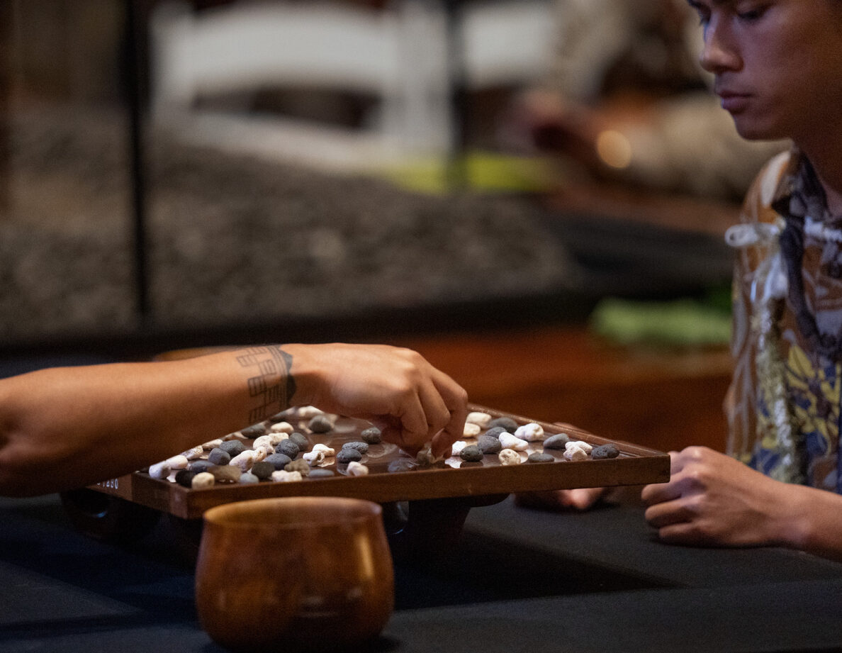 An all-Oʻahu championship match between Kapena Baptista, right, makes a move under the watchful eyes of Kahekili Yung, during the inaugural Ka Makou Kōnane Invitational Tournament in the center of the Bishop Museum’s Hawaiʻian Hall Friday, Feb. 13, 2026, in Honolulu. (Kevin Fujii/Civil Beat/2026)