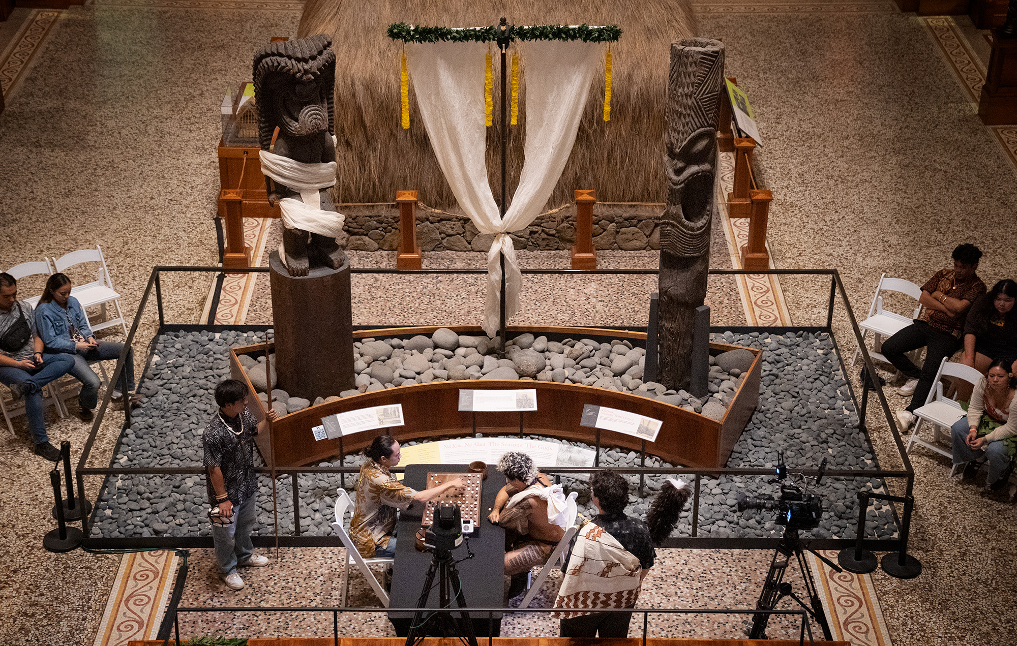 Ki‘i dressed for Makahiki watch over an all-Oʻahu championship match between Kahekili Yung, left, and Kapena Baptista during the inaugural Ka Makou Kōnane Invitational Tournament takes place at the Bishop Museum Friday, Feb. 13, 2026, in Honolulu. (Kevin Fujii/Civil Beat/2026)