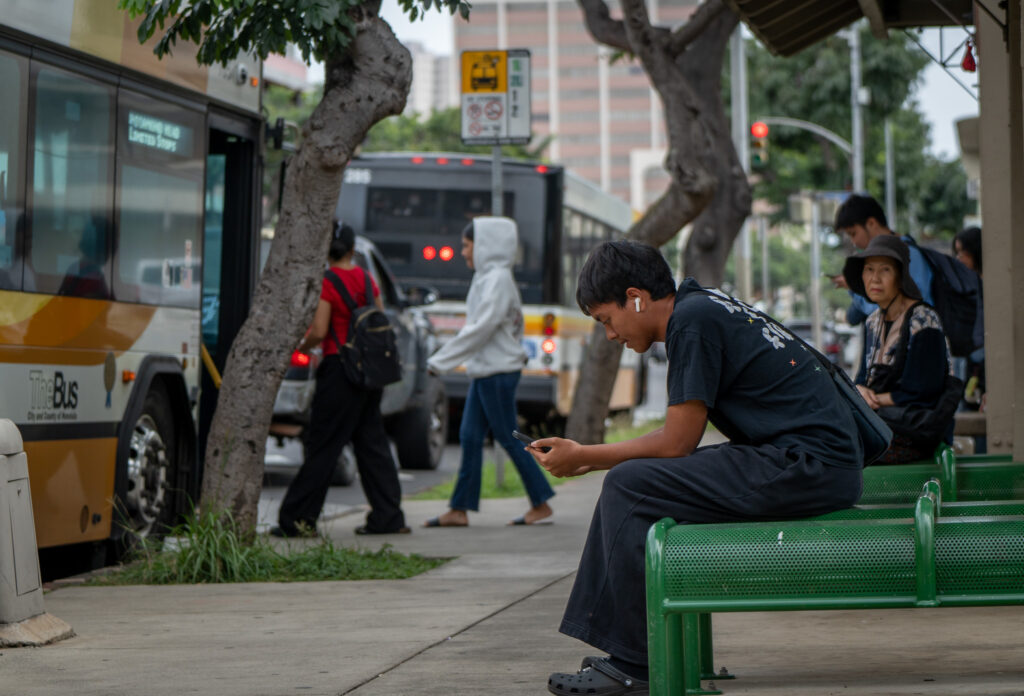 McKinley High School senior Aldrich Perez looks at his phone waiting for his bus in Honolulu, Thursday, Feb. 19, 2026. (Craig Fujii for Civil Beat). Perez is making plans to study accounting or nursing.
