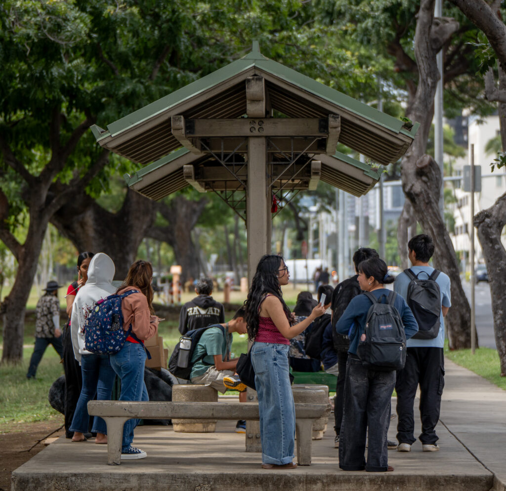 Bus riders, several from McKinley High School, wait at the bus stop at King and Pensacola Sts in Honolulu, Thursday, Feb. 19, 2026. (Craig Fujii for Civil Beat)