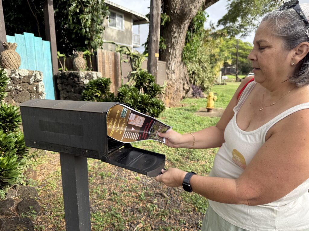 Kōloa resident Rita Norman places a flier about the Feb. 18 meeting about the proposed housing project in a neighbor’s mailbox. (Noelle Fujii-Oride/Civil Beat/2026)
