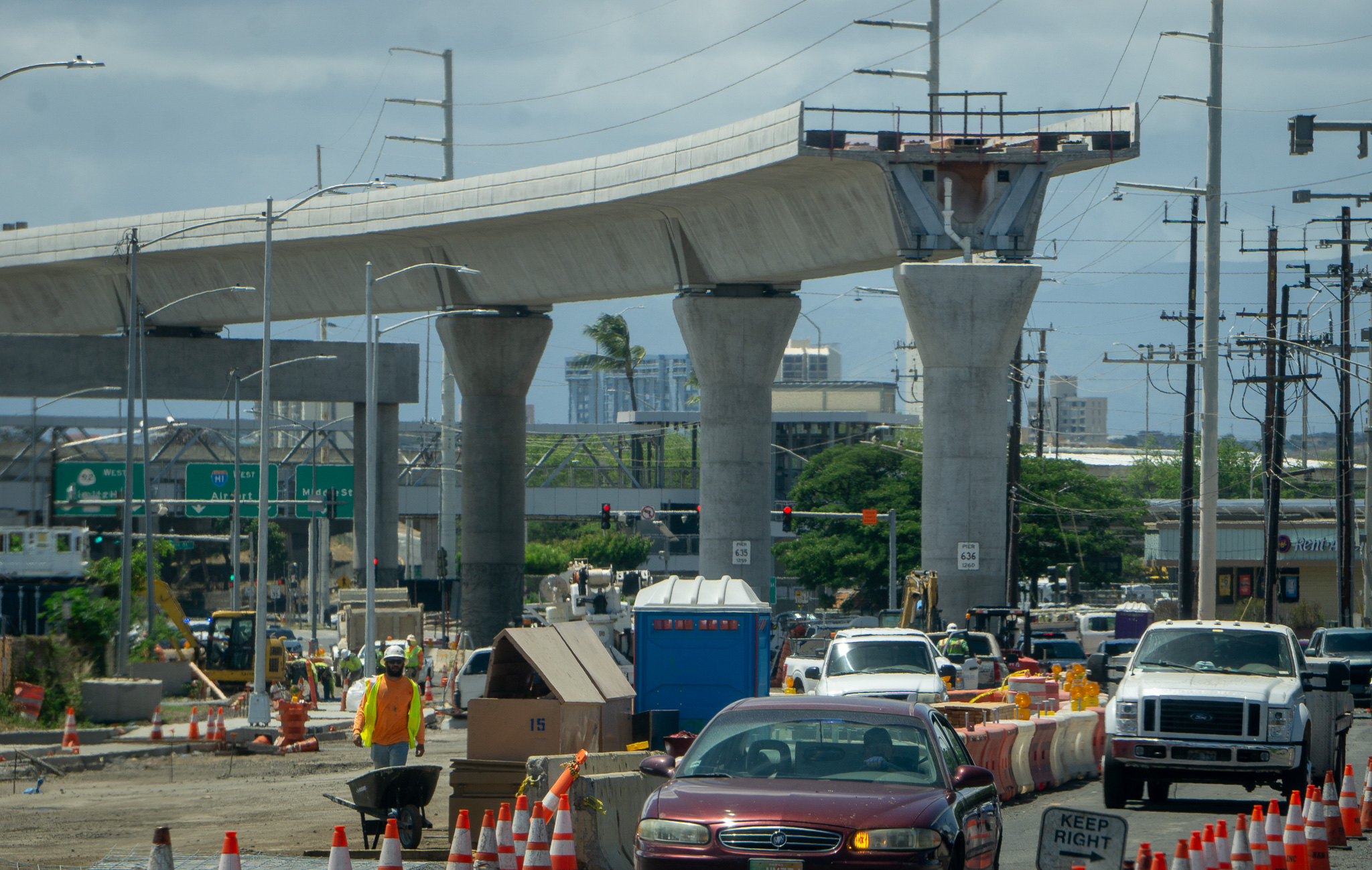 An elevated railway under construction with vehicles and construction objects in the foreground.