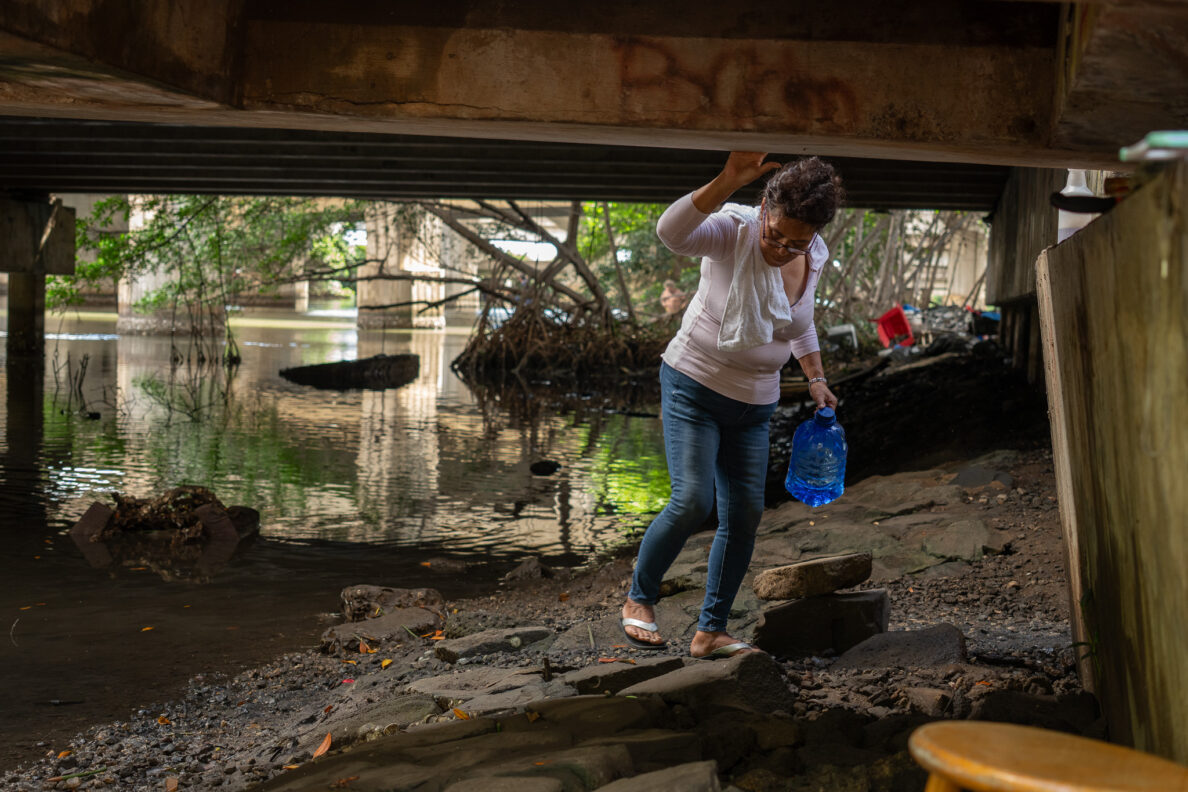 Kim Mathias steps gingerly on pavement stones under a bridge next to a saltwater stream near Ke'ehi Transfer Station. Mathias has been camping in a tent under the bridge for almost one year. She has been clearing the stream bank of debris and trash, falling into the muck several times while doing so. She has seen a spotted eagle ray swimming in the shallow waters at that site.