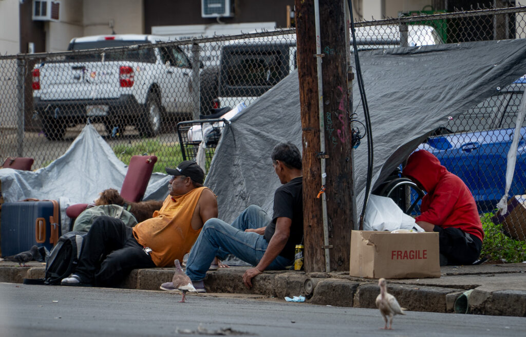 14:43 Men sitting on a sidewalk next to Punawai Rest Stop in Iwilei, Monday. The rest stop provides hygiene facilities, cellphone charging, laundry and social services.