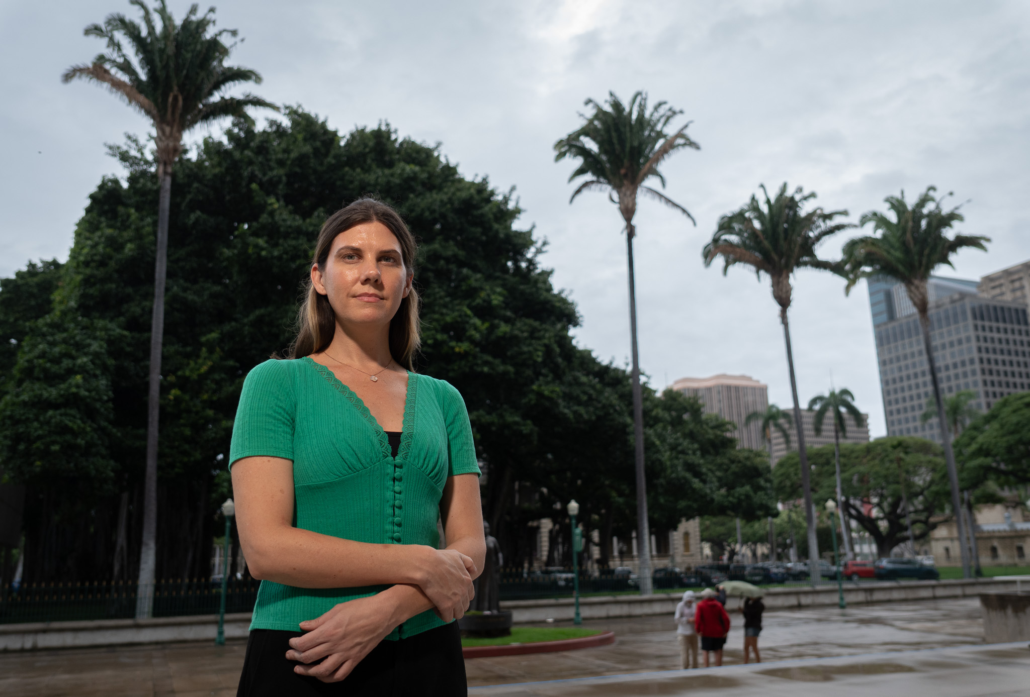 A woman with a green top is photographed with a large tree and four palm trees in the background.