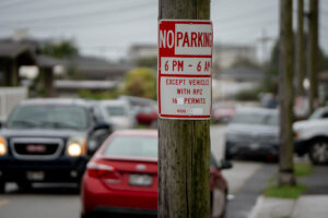 A no parking sign on a telephone phone with cars in the background out of focus.