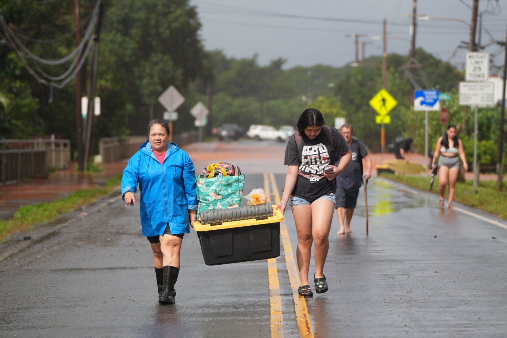 People carry their belongings down Waialua Beach Road, Friday. (Craig Fujii/Civil Beat/2026)